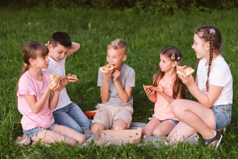 Dzieci wspólnie jedzą pizzę podczas warsztatów kulinarnych dla szkół organizowanych przez Górską Akademię